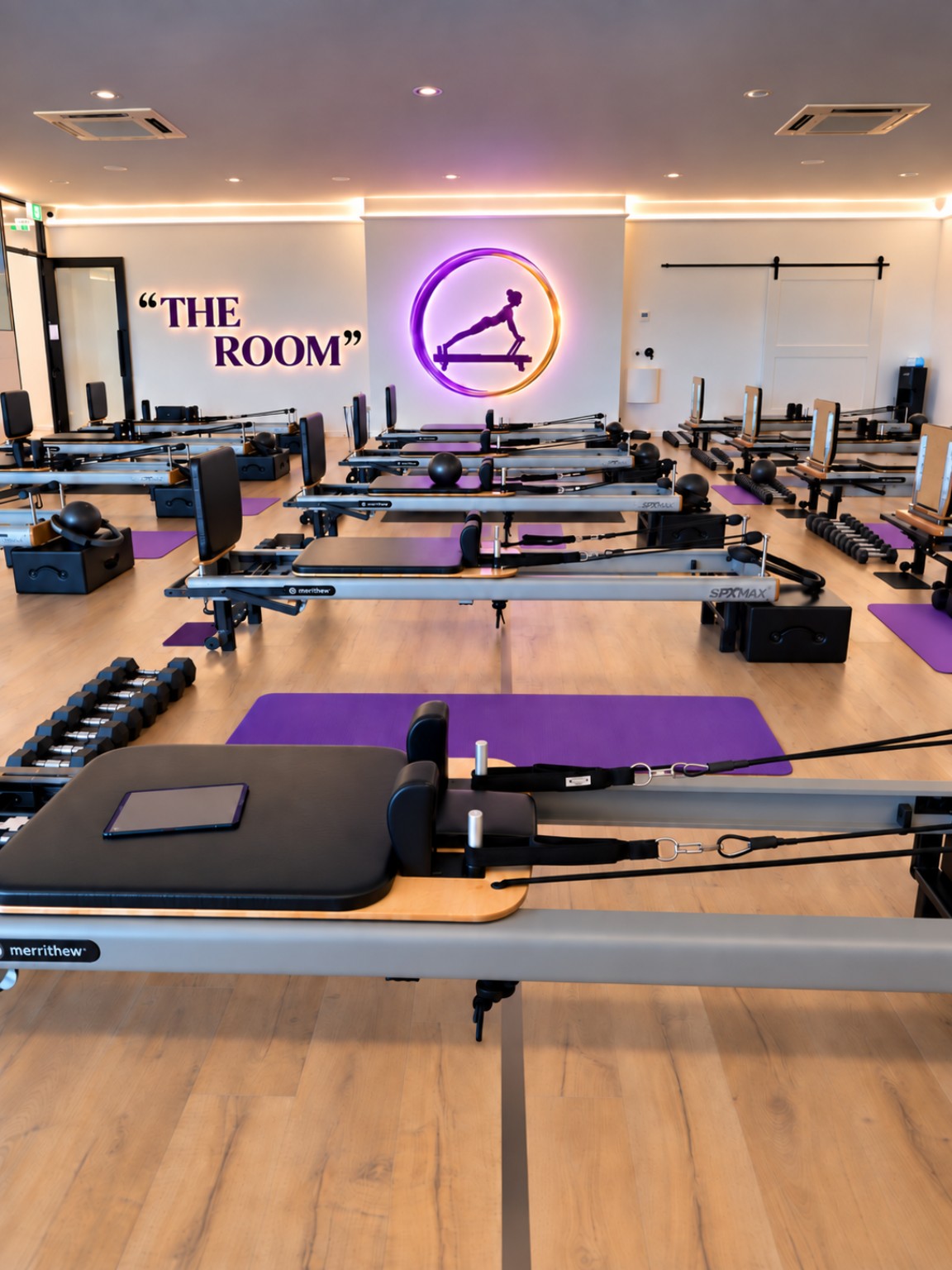 Reformers, dumbbells and orchid purple mats on the studio floor